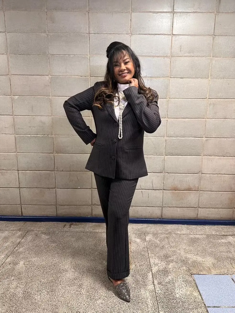 Solange Couto é uma mulher negra de pele clara, idosa, cabelo castanho ondulado e com uma franja. Na foto, ela usa terno cinza e camisa branca por baixo.