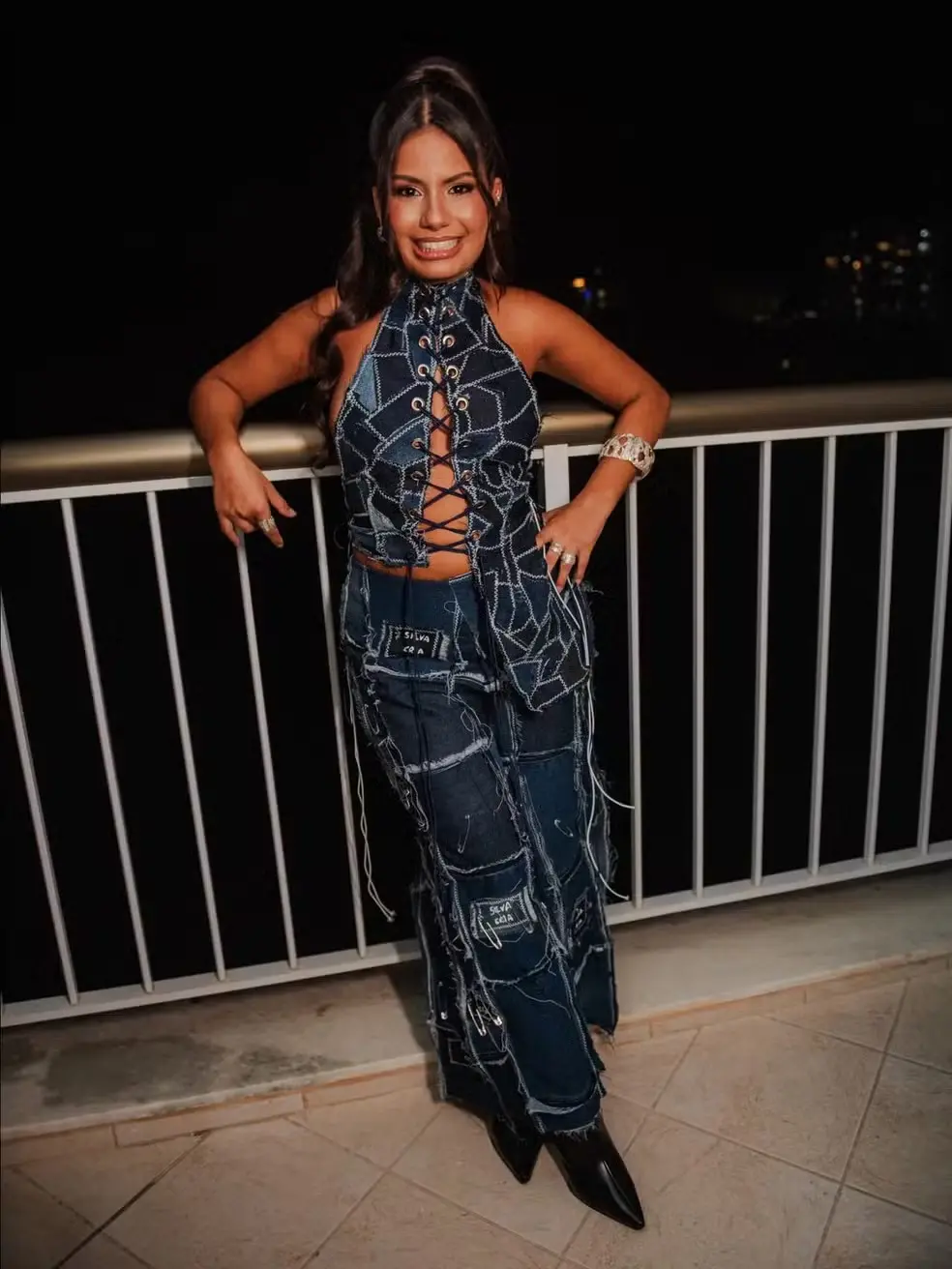 Gabriela é uma mulher jovem negra de pele clara e na foto usa uma blusa jeans amarrada com uma calça da mesma estampa.