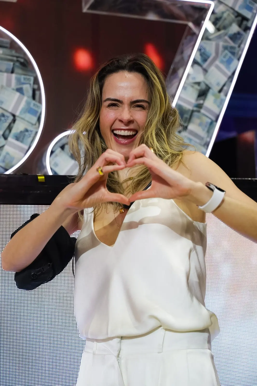 Ana Paula Renault sentada em ambiente interno do BBB 26, vista de perfil, com cabelo solto, vestindo blusa de alça; logotipo do programa aparece no canto superior da imagem.