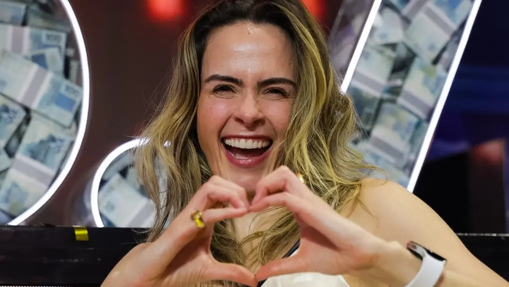 Ana Paula Renault sentada em ambiente interno do BBB 26, vista de perfil, com cabelo solto, vestindo blusa de alça; logotipo do programa aparece no canto superior da imagem.