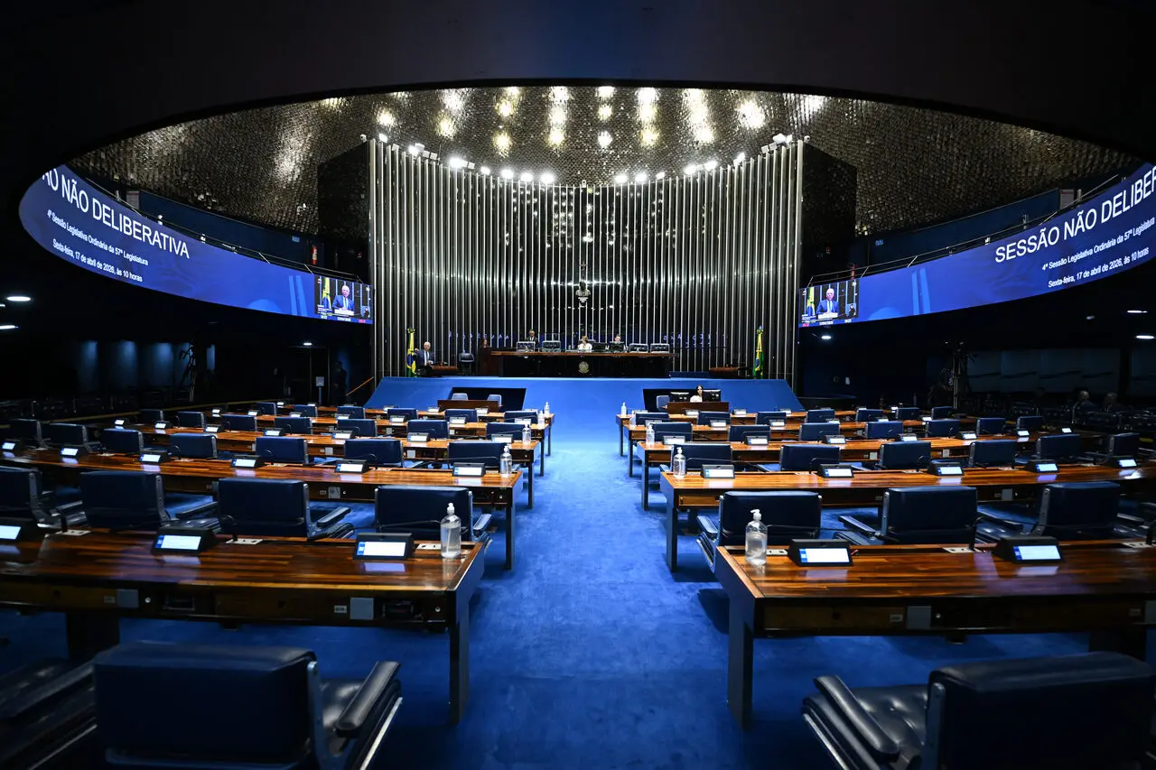 Interior do plenário, com chão azul, bancadas de madeira e luminosidade ao centro.
