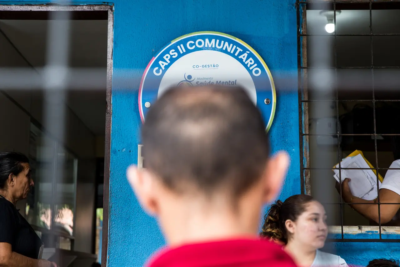 Imagem mostra uma clínica de saúde mental com o símbolo do CAPS II Comunitário, onde pessoas aguardam atendimento na entrada, destacando a importância do cuidado com a saúde mental na comunidade.
