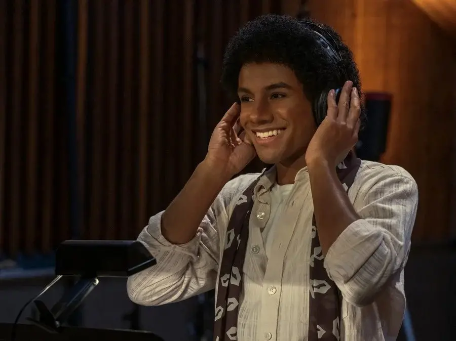 Jovem sorridente usando fones de ouvido em um estúdio de gravação, representando criatividade musical e sucesso na produção artística.