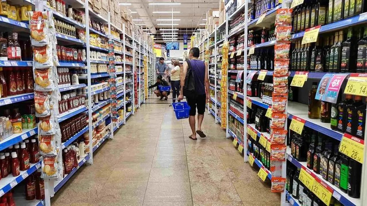 Vista de um corredor de um supermercado com um cliente com uma cesta na mão em primeiro plano.