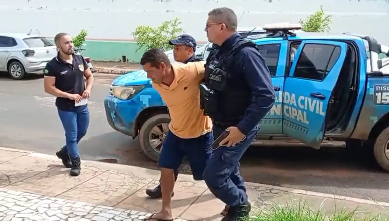 Agentes da Guarda Civil de Deputado Irapuan Pinheiro conduzem um homem algemado em direção a uma viatura azul estacionada em uma via pública. A imagem registra a movimentação policial em plena luz do dia, com outros oficiais acompanhando a ação próximo à calçada.