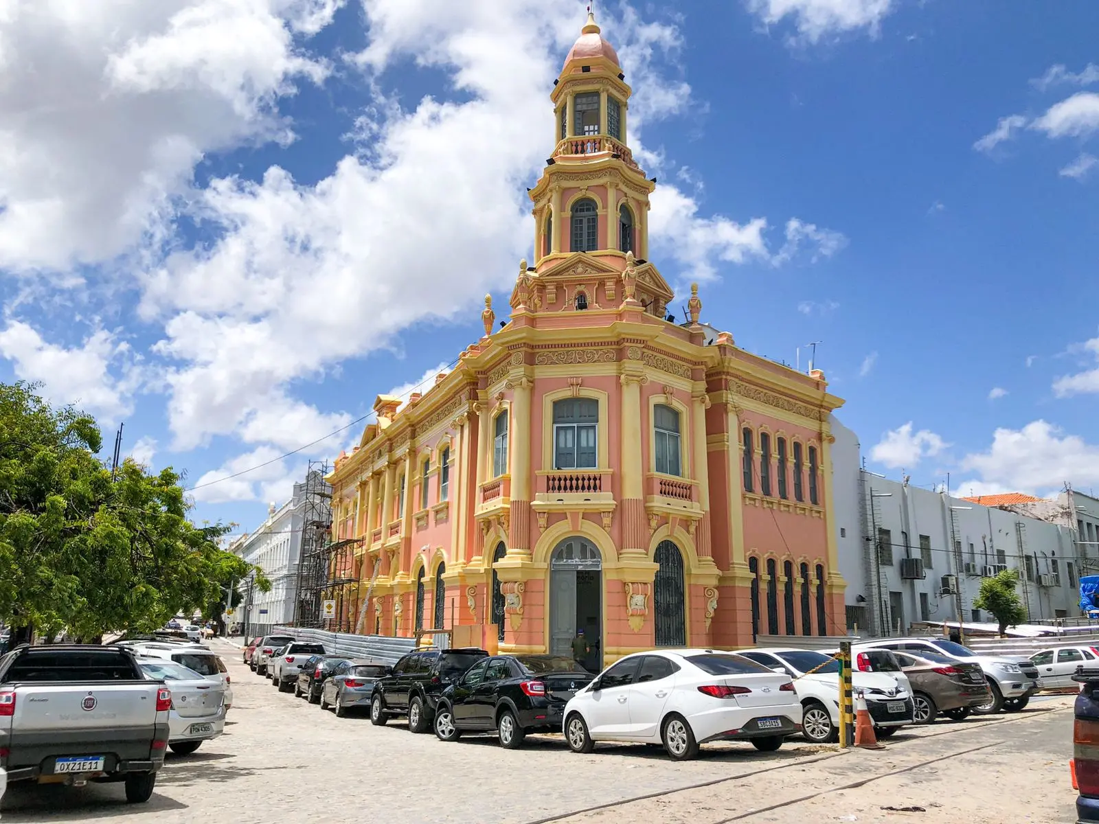 Edifício colorido de arquitetura histórica, localizado na cidade de Salvador, Bahia, com céu azul ao fundo e carros estacionados em frente.