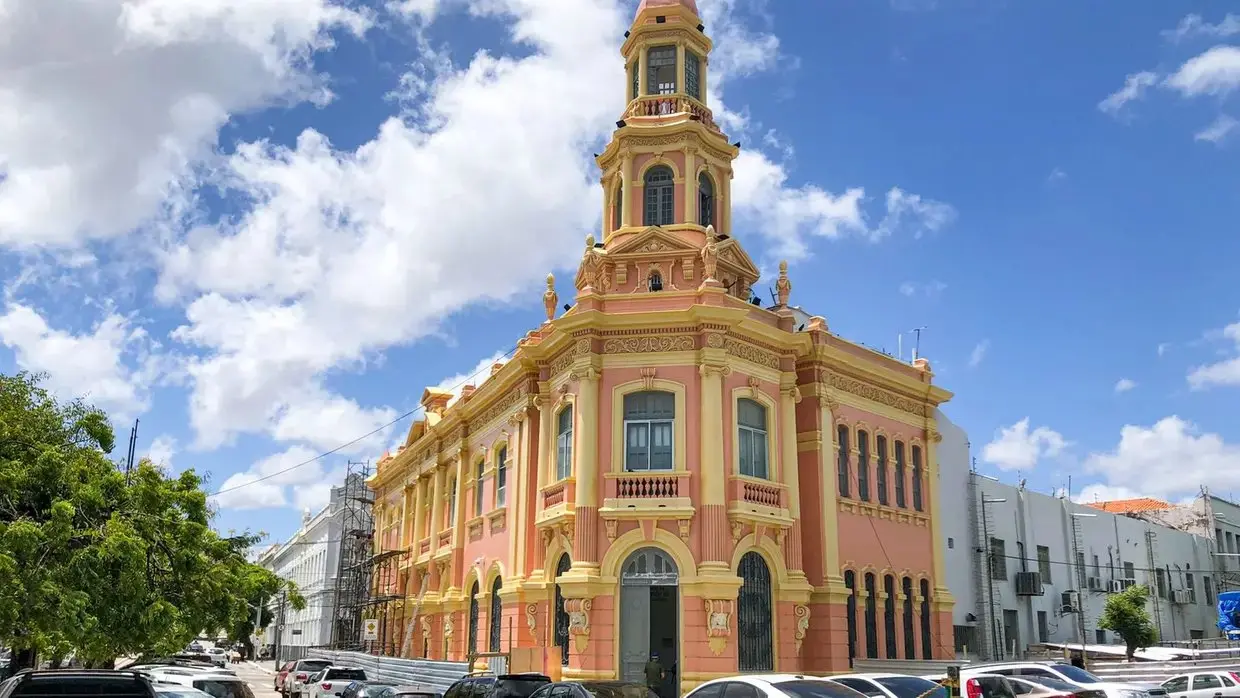 Edifício colorido de arquitetura histórica, localizado na cidade de Salvador, Bahia, com céu azul ao fundo e carros estacionados em frente.