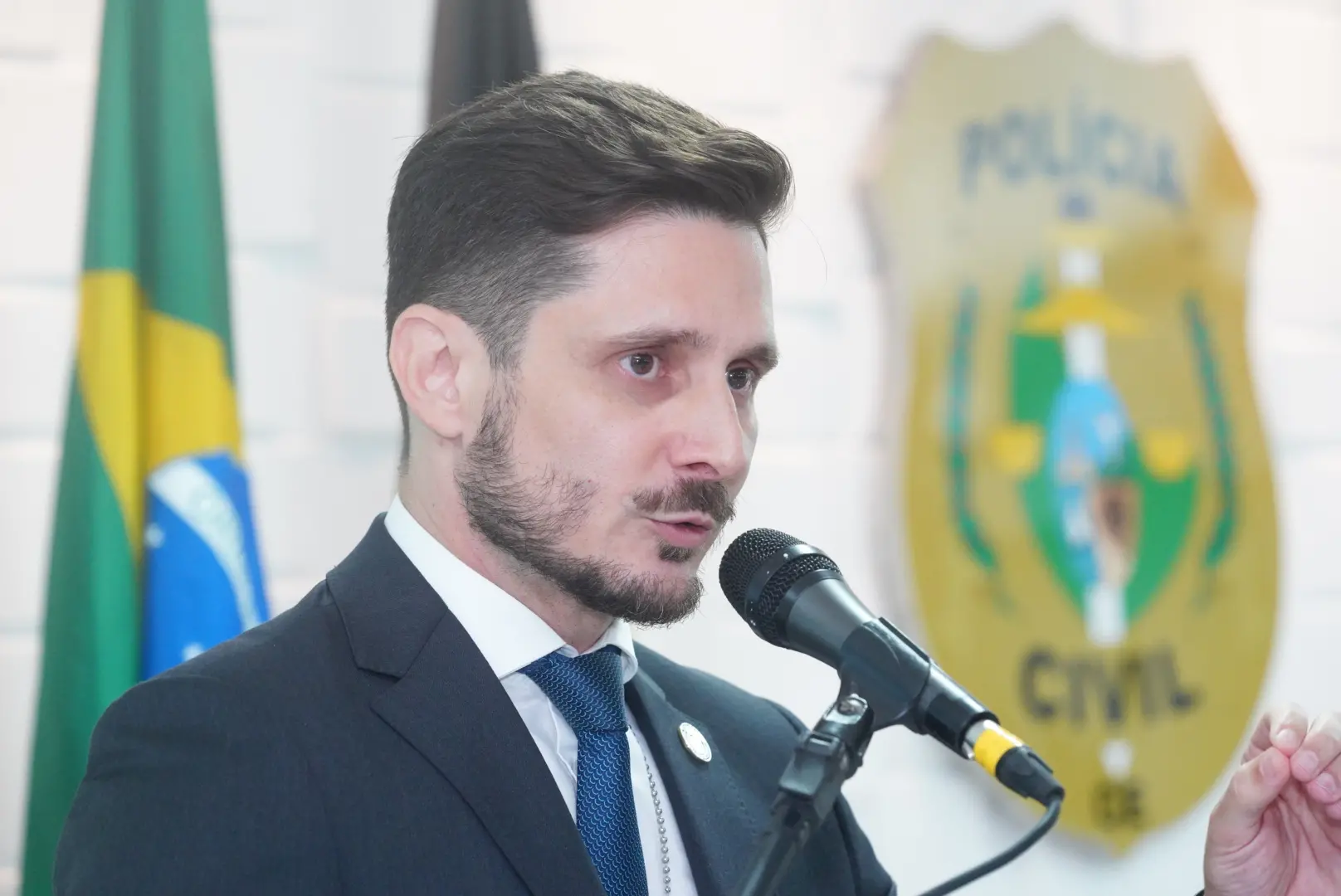 delegado-geral marcio gutierrez falando ao microfone, simbolo policia civil do ceará.
