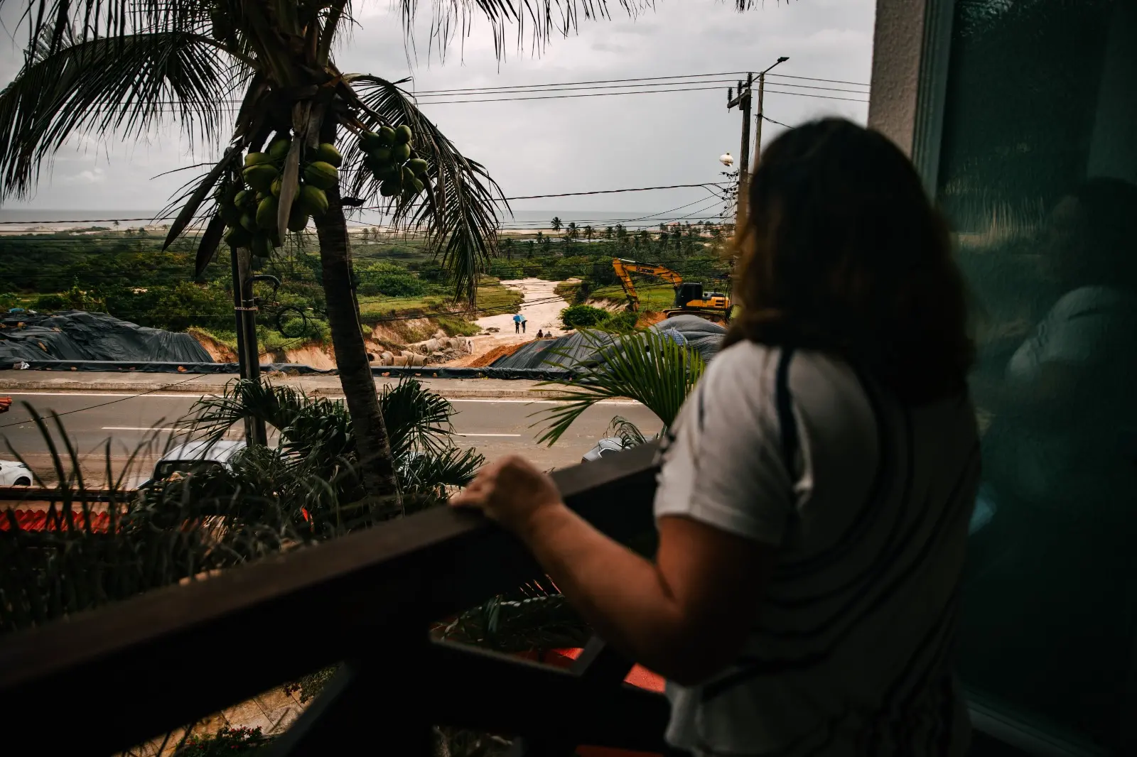 Imagem mostra moradora de condomínio assistindo trabalhadores recuperarem asfalto após cratera abrir na ce-025 em Aquiraz.