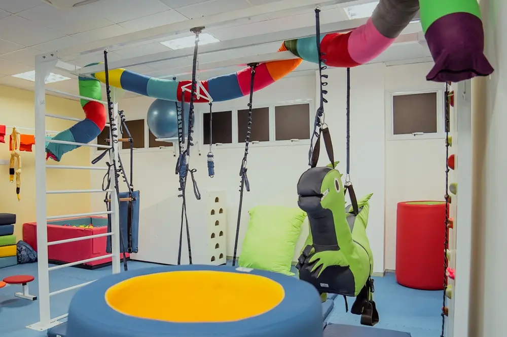 Sala terapêutica sensorial com equipamentos suspensos coloridos, balanços e estruturas de estímulo motor no novo Espaço Girassol