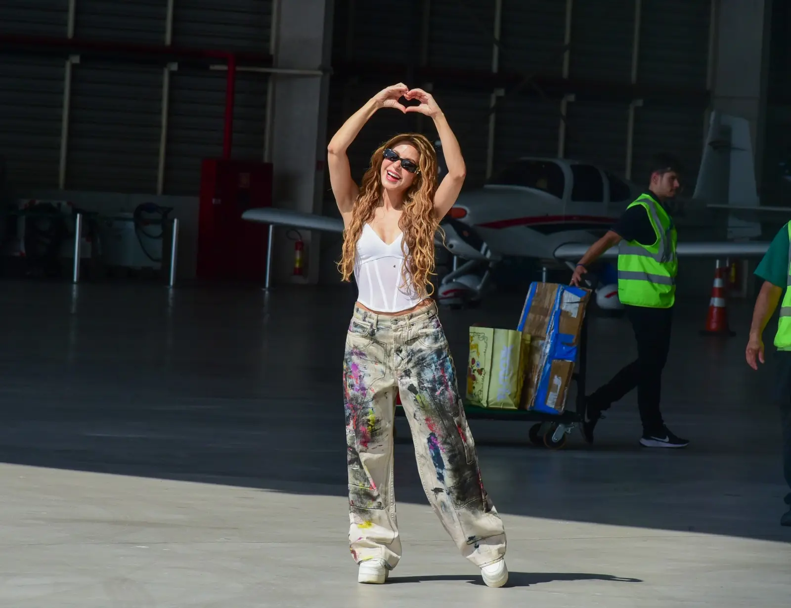 fotos de Shakira desembarcando no Rio de Janeiro para show em Copacabana. A cantora usa corpete branco, calça jeans estilizada e tênis.