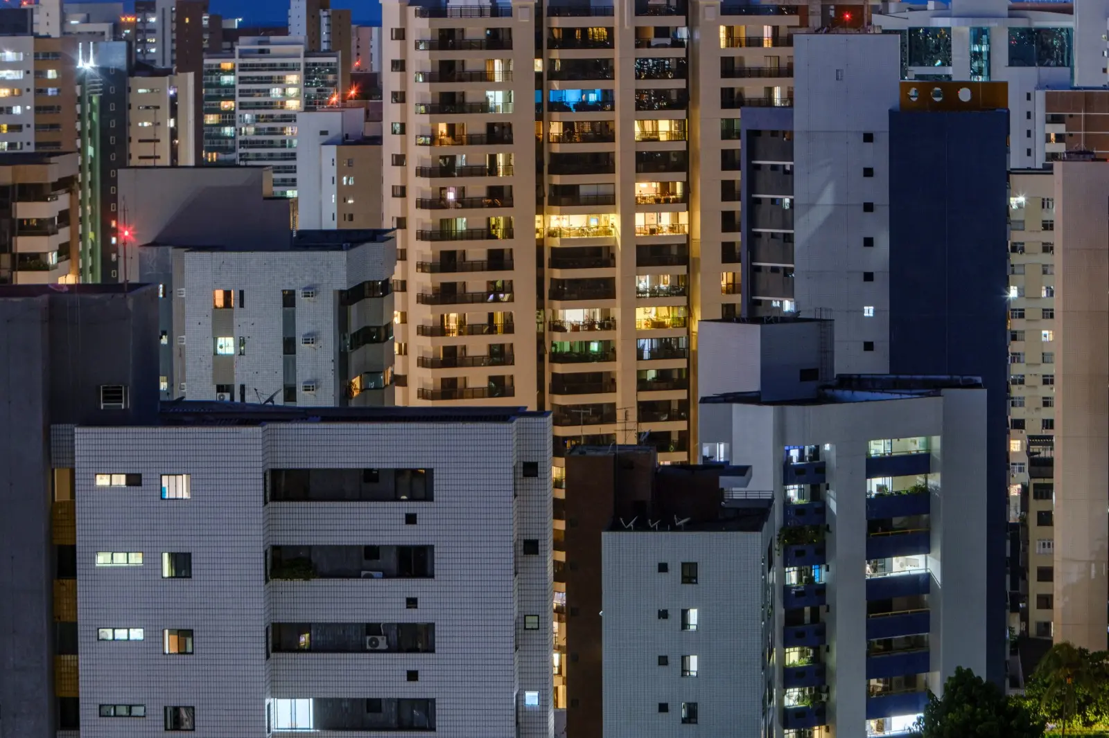 Foto que contém fachadas de vários prédios de apartamentos em Fortaleza. Luzes estão acesas em vários deles.