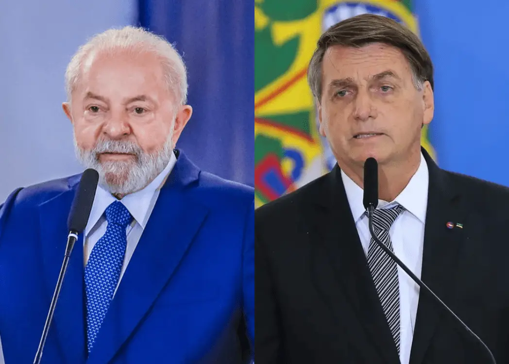 Imagem dividida ao meio mostra dois políticos brasileiros falando ao microfone. À esquerda, Luiz Inácio Lula da Silva aparece de terno azul, gravata azul e fundo em tom azulado, com expressão séria. À direita, Jair Bolsonaro está de terno escuro e gravata listrada, diante de um fundo com as cores da bandeira do Brasil, também com expressão séria, ambos em posição de discurso.