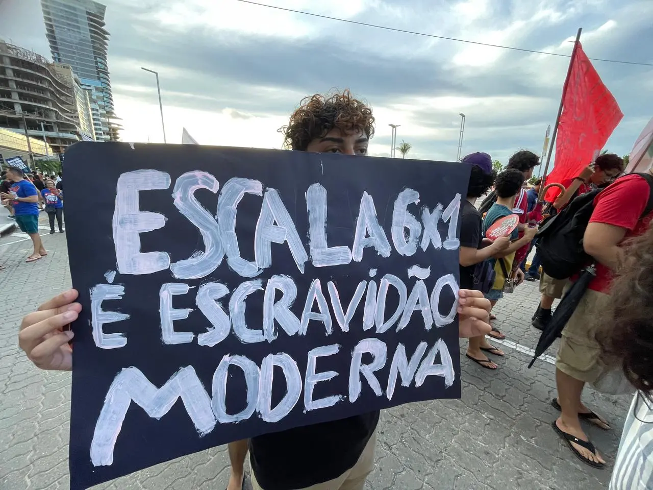 Jovem segura cartaz preto com a frase 