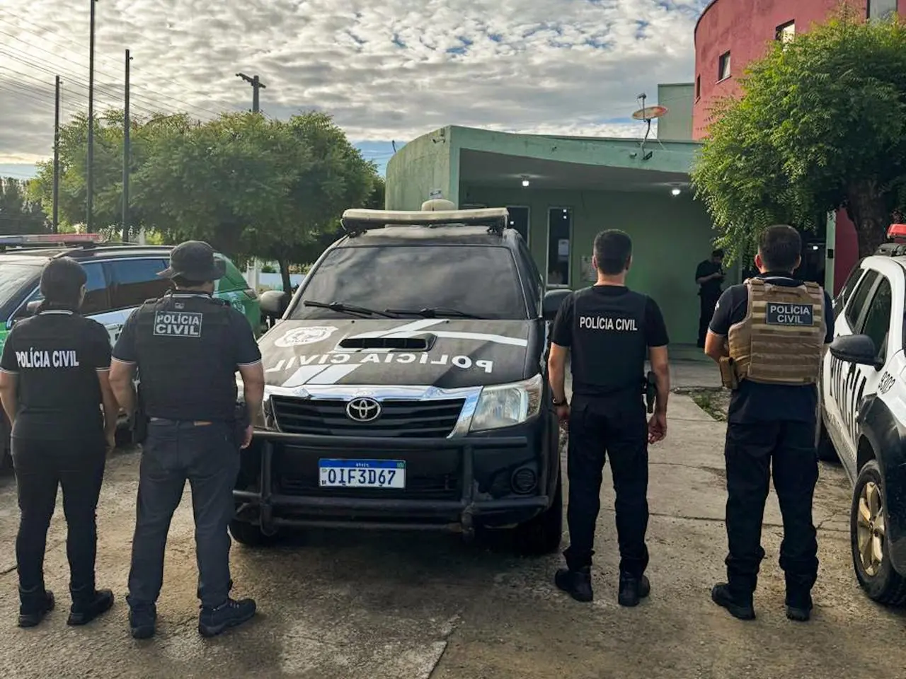 agentes da polícia civil, de costas, ao lado de viatura.