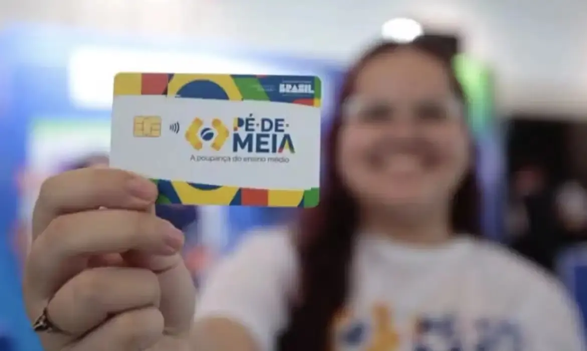Uma jovem sorridente segura em primeiro plano o cartão do programa 