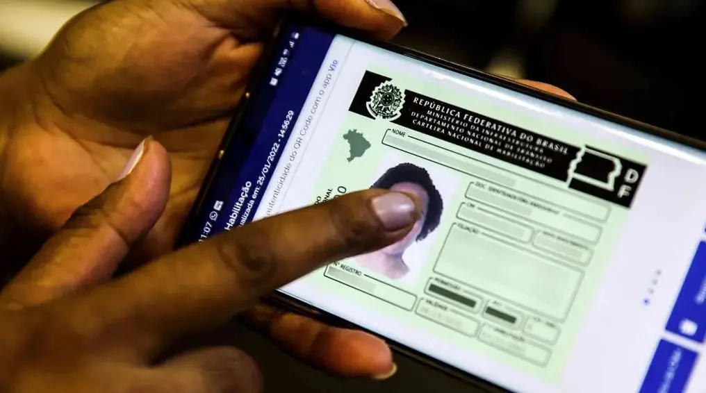 Mão segura um smartphone exibindo a versão digital da Carteira Nacional de Habilitação do Brasil na tela.