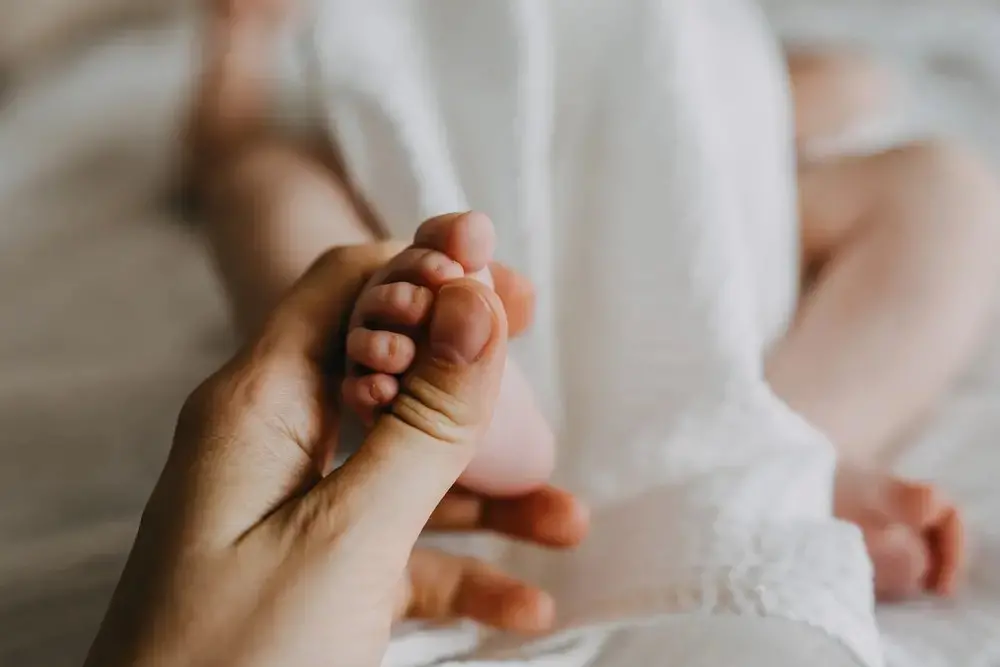 Imagem mostra mão de uma mulher segurando o pé de um bebê.