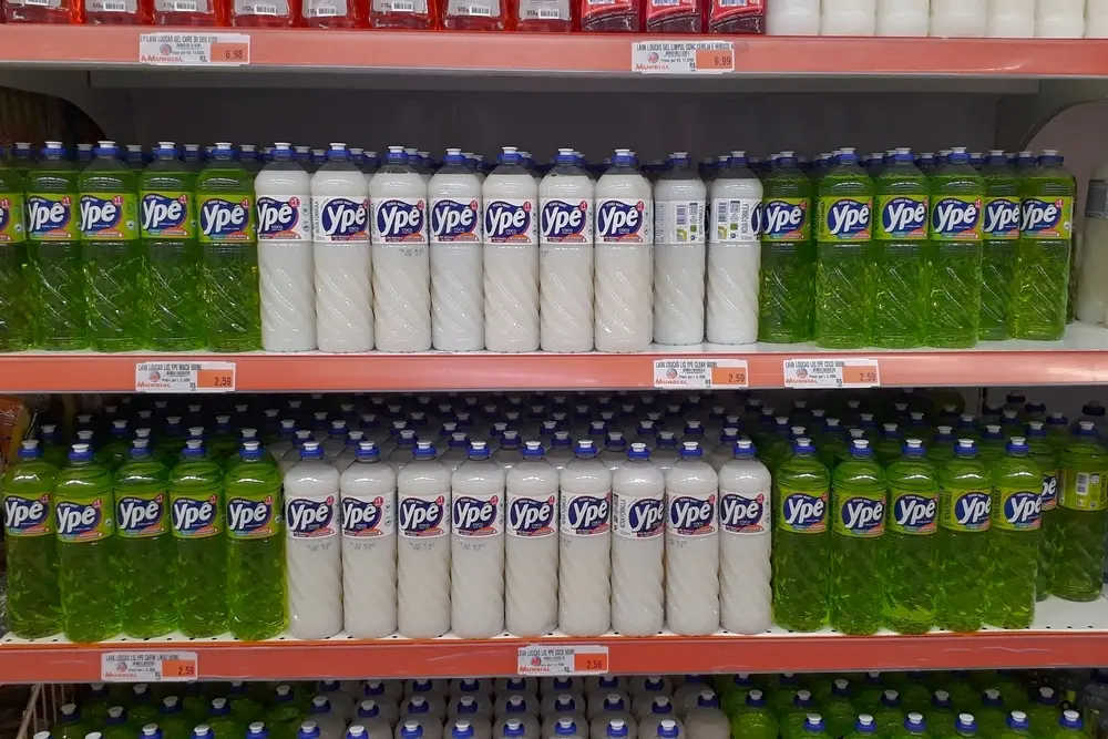 Varejo com várias garrafas de detergente Ypê na prateleira de supermercado, exibindo embalagens verdes e brancas, ideal para limpeza doméstica.