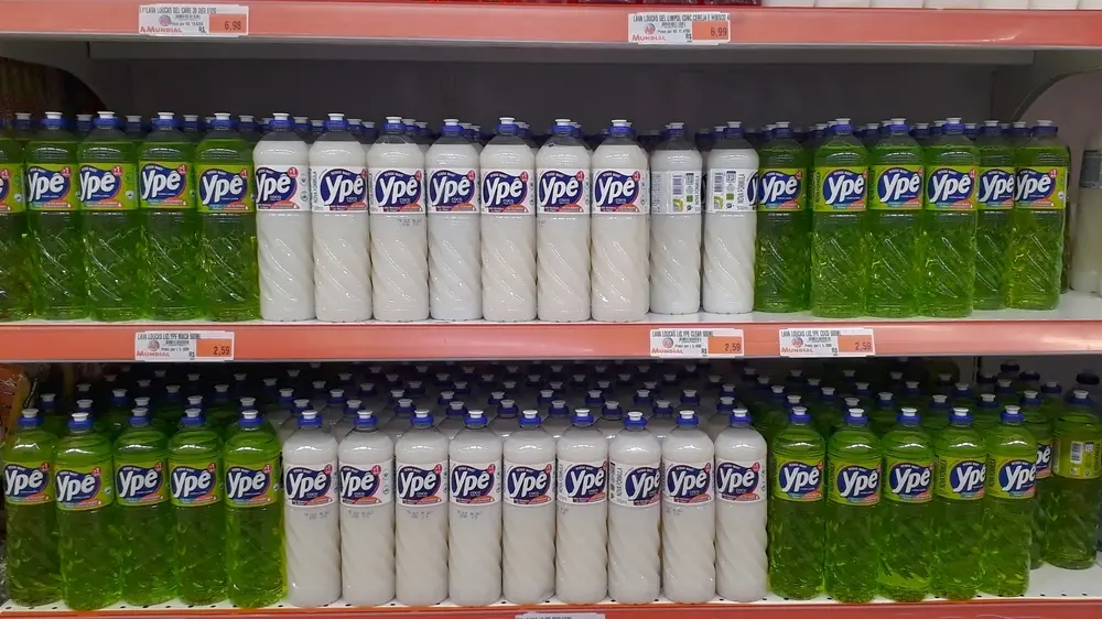 Varejo com várias garrafas de detergente Ypê na prateleira de supermercado, exibindo embalagens verdes e brancas, ideal para limpeza doméstica.