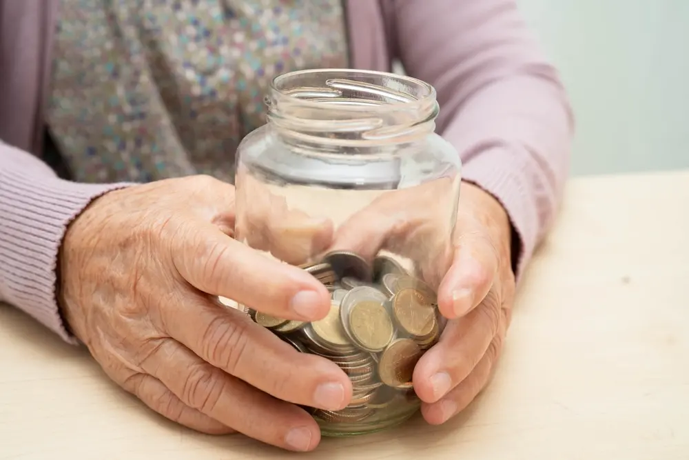 Idosa segurando frasco de vidro com moedas, símbolo de economia e finanças pessoais para otimizar economia doméstica.