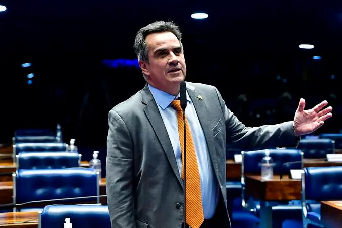 O senador Ciro Nogueira discursa no plenário do Senado Federal, vestindo paletó cinza e gravata alaranjada enquanto gesticula com a mão esquerda aberta. Ao fundo, as poltronas azuis vazias e a iluminação pontual do ambiente compõem o cenário legislativo em um ângulo de meio corpo.