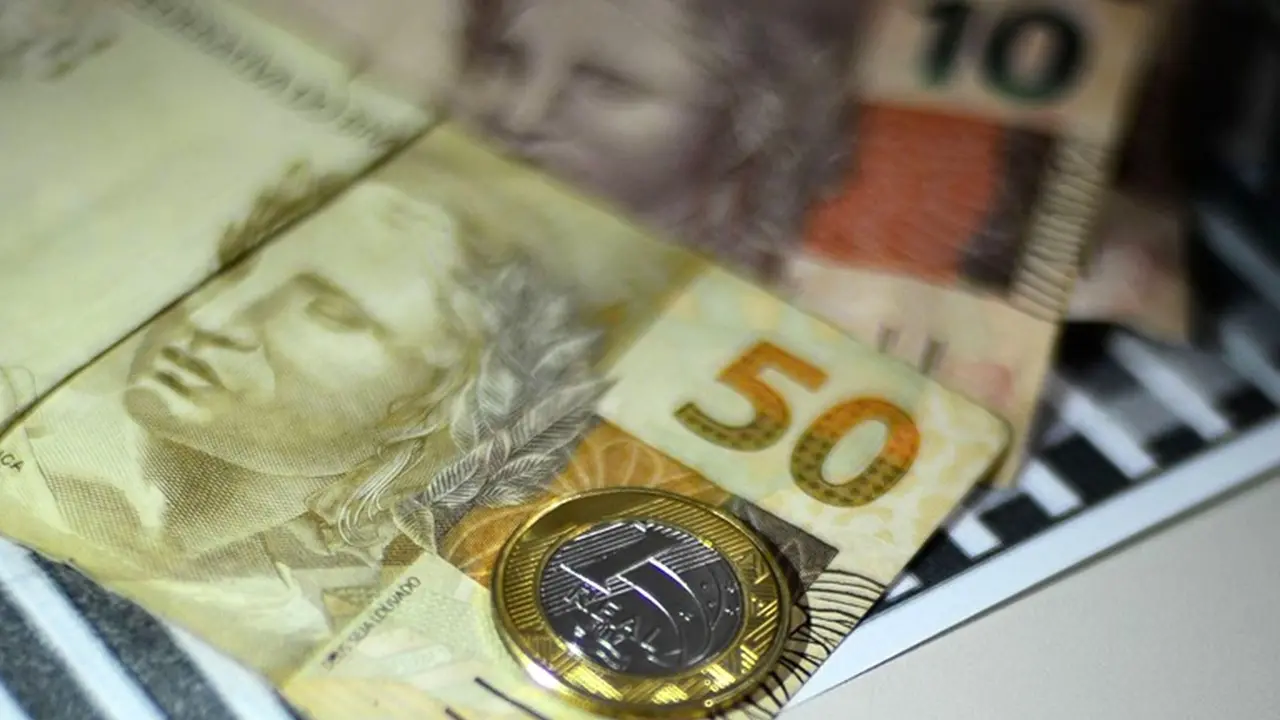 Cédulas e moeda de real sobre calculadora representam renda, consumo e movimentação da economia brasileira.