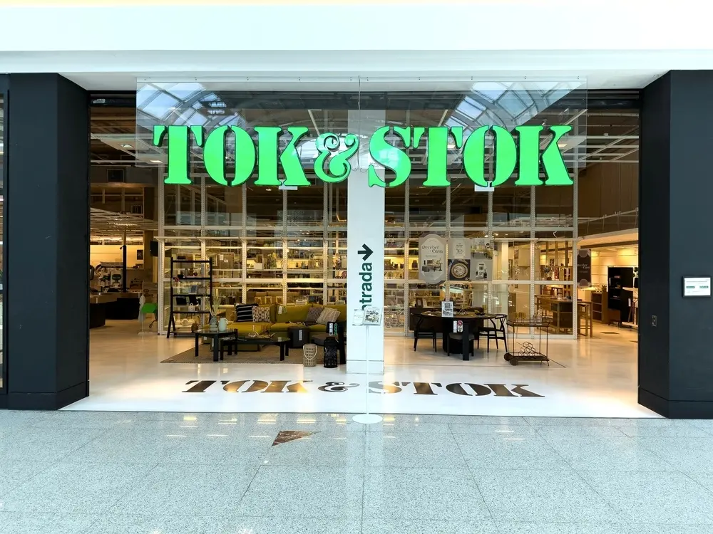Fachada da Tok&Stok, uma loja de móveis e decoração para casa, com grande sinalização verde e portas de vidro que revelam os produtos expostos no interior.