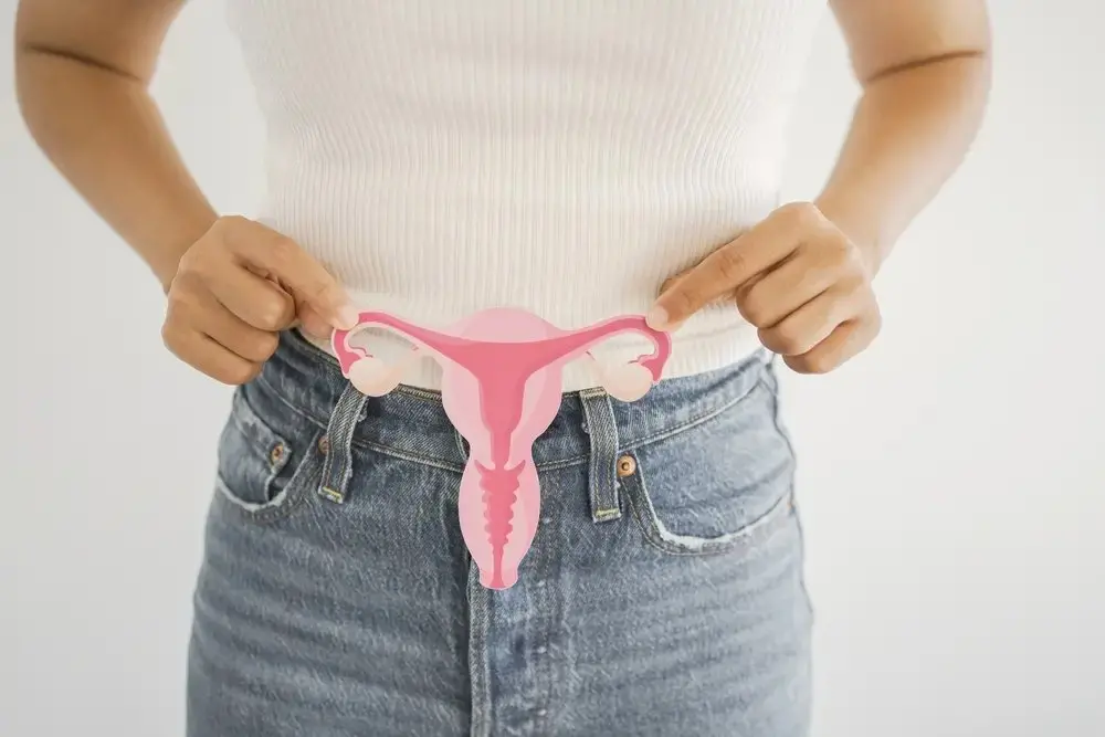 foto de mulher segurando imagem de útero. Ela usa calça jeans e blusa branca. Imagem usada em matéria sobre novo nome da Síndrome dos Ovários Policísticos (SOP).