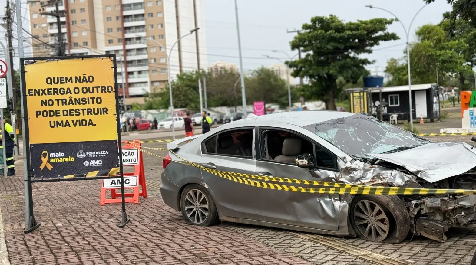 Placa de conscientização de trânsito ao lado de veículo danificado.