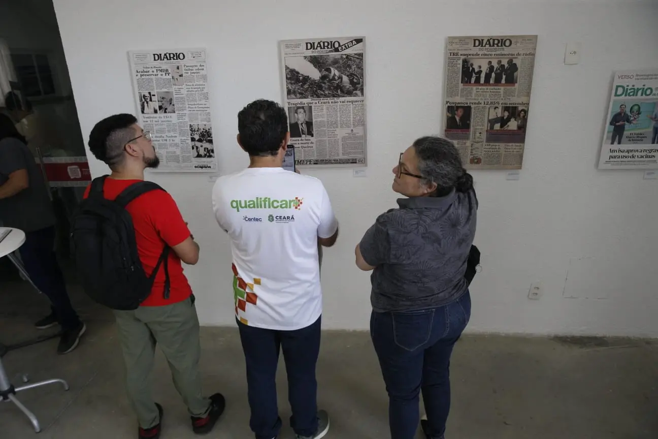 pessoas de costas, diante de painel de exposição.