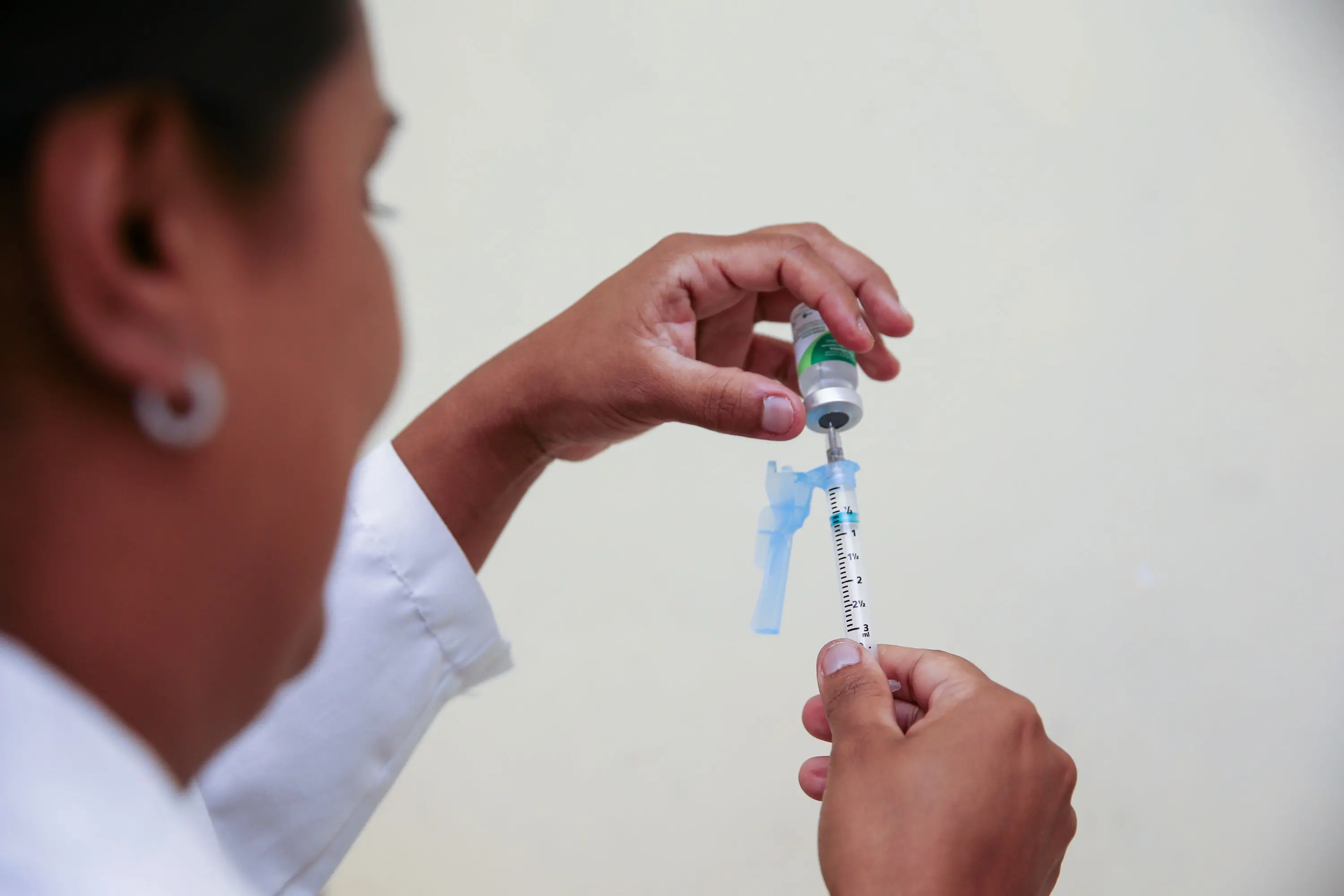 pessoa colocando vacina de influenza em seringa. profissional de saúde está de costas e o foco está nas mãos e na seringa.