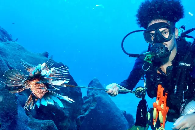 foto de pesquisador em contato com peixe-leão durante missão marinha.