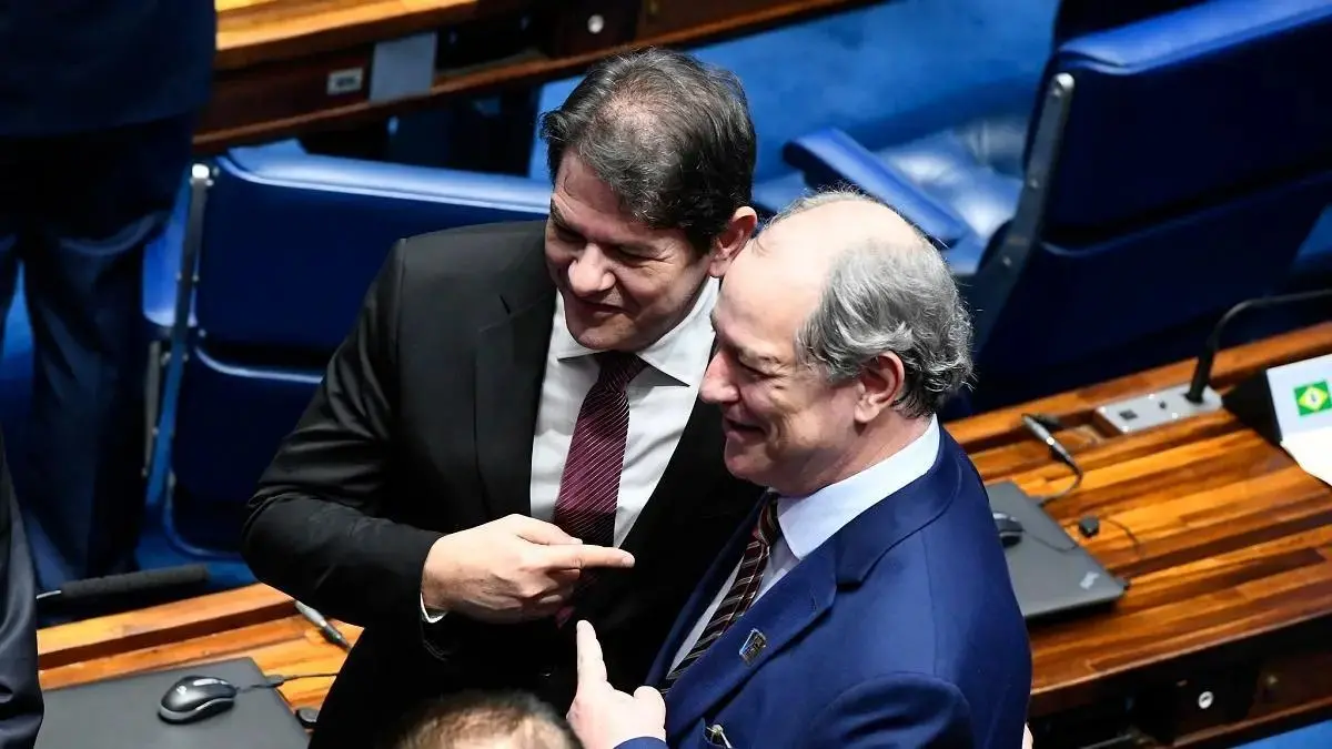 Os irmãos Cid e Ciro Gomes conversam e sorriem durante sessão no Senado Federal. Ambos usam terno e aparecem próximos às bancadas do plenário.