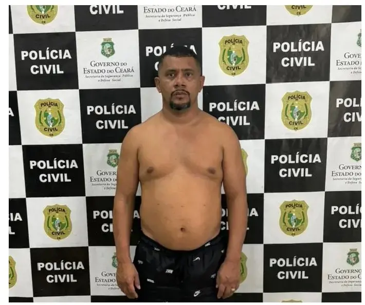 Homem detido em pé diante de painel da Polícia Civil do Ceará com logomarcas oficiais ao fundo durante registro policial.