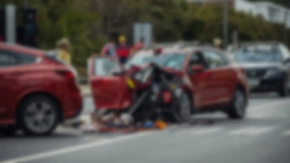 Imagem desfocada representando uma cena de acidente de carro com veículos danificados, socorristas de emergência e as consequências de uma colisão em uma estrada.
