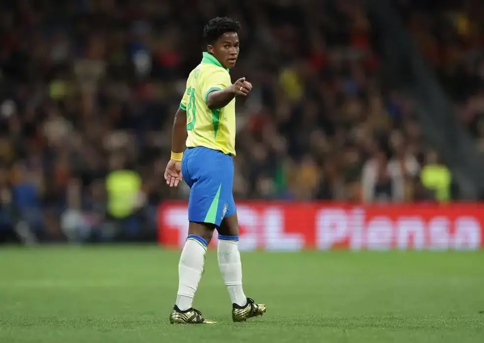 Jogador Endrik, o convocado mais novo para a Copa do Mundo de 2026 desde Ronaldo, está em pé, de levimente de costas, no campo de futebol com o uniforme da Seleção Brasileira.