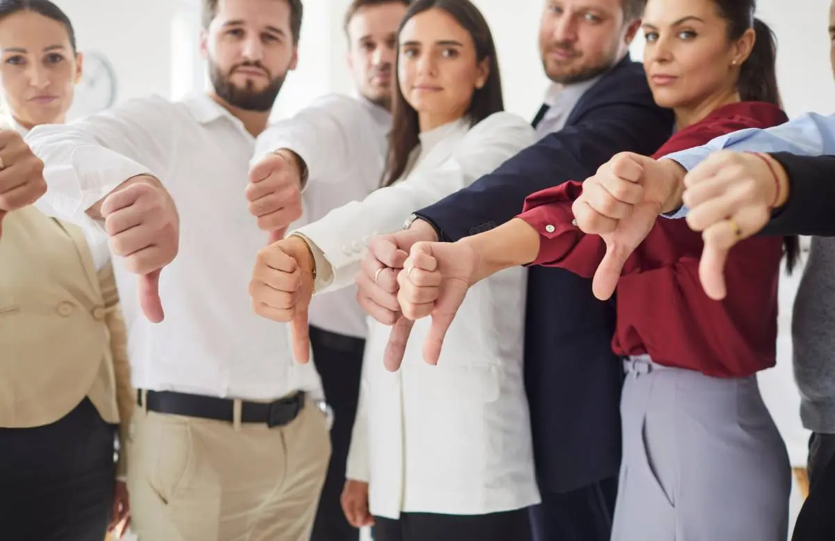 Um grupo de pessoas brancas com trajes corporativos fazendo um sinal de negativo para demonstrar insatisfação.
