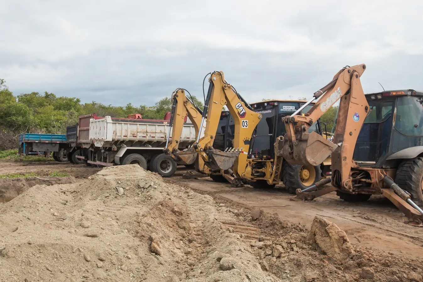 Foto que contém tratores e caminhões em canteiro de obras de Quixeramobim.