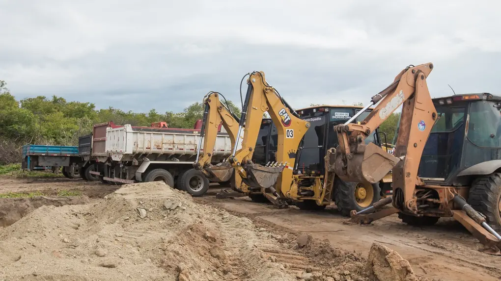 Foto que contém tratores e caminhões em canteiro de obras de Quixeramobim.