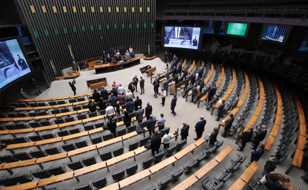 Imagem aérea de Plenário da Câmara, com mesas de madeira semicirculares e alguns deputados.