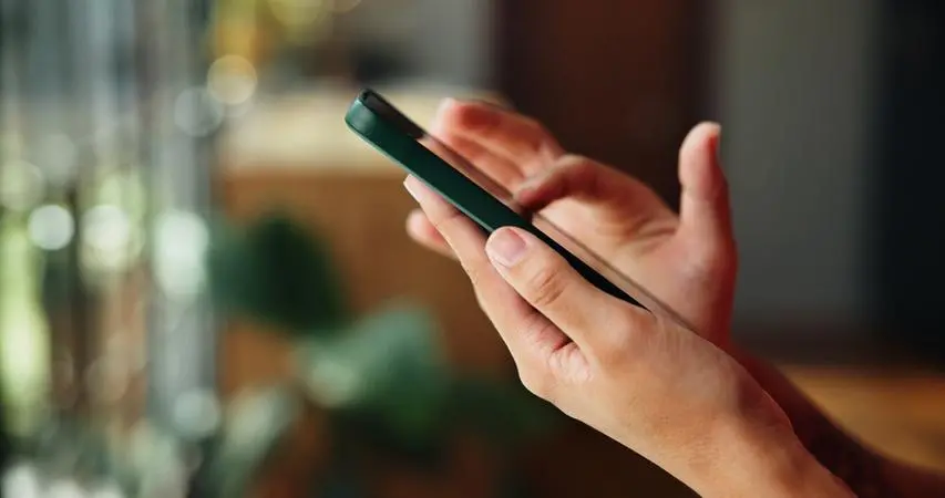 Mão de pessoa branca segurando um celular e deslizando o dedo sobre a tela.