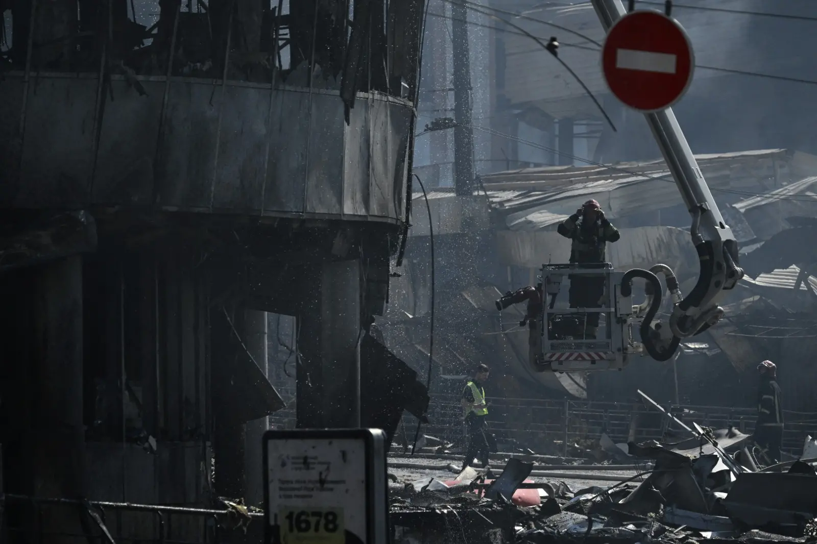 Equipes de resgate ucranianas operam no local de um shopping center gravemente danificado, enquanto fumaça sobe ao fundo, após ataques russos em Kiev em 24 de maio de 2026, em meio à invasão russa da Ucrânia