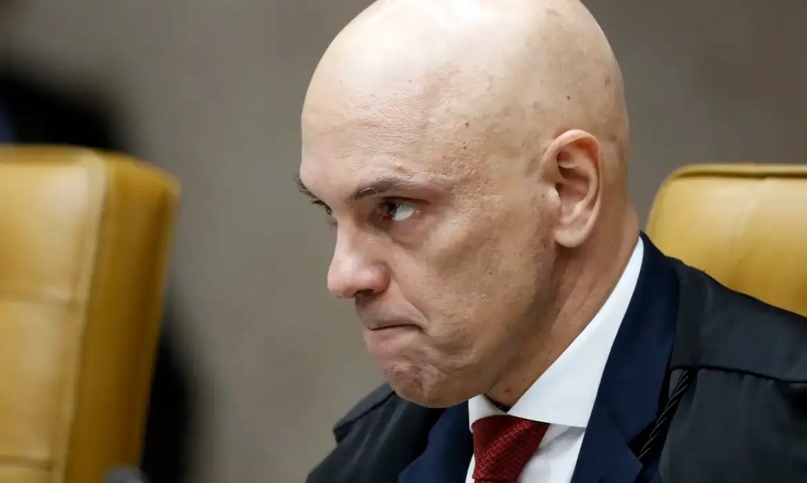 Imagem em close do ministro do STF, Alexandre de Moraes, de perfil, usando terno escuro, camisa branca e gravata vermelha, no plenário do Supremo Tribunal Federal, em Brasília.