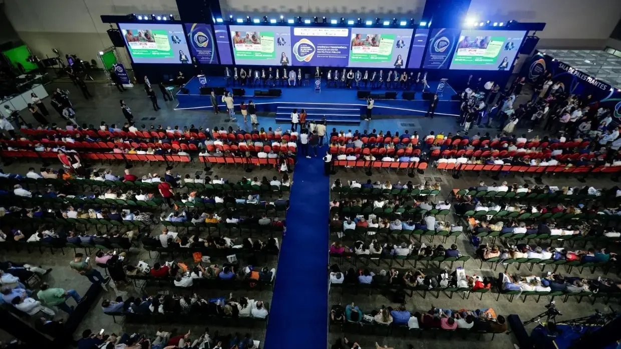 Imagem mostra palco com dezenas de espectadores que assistem a palestras do Seminário de Prefeitos.