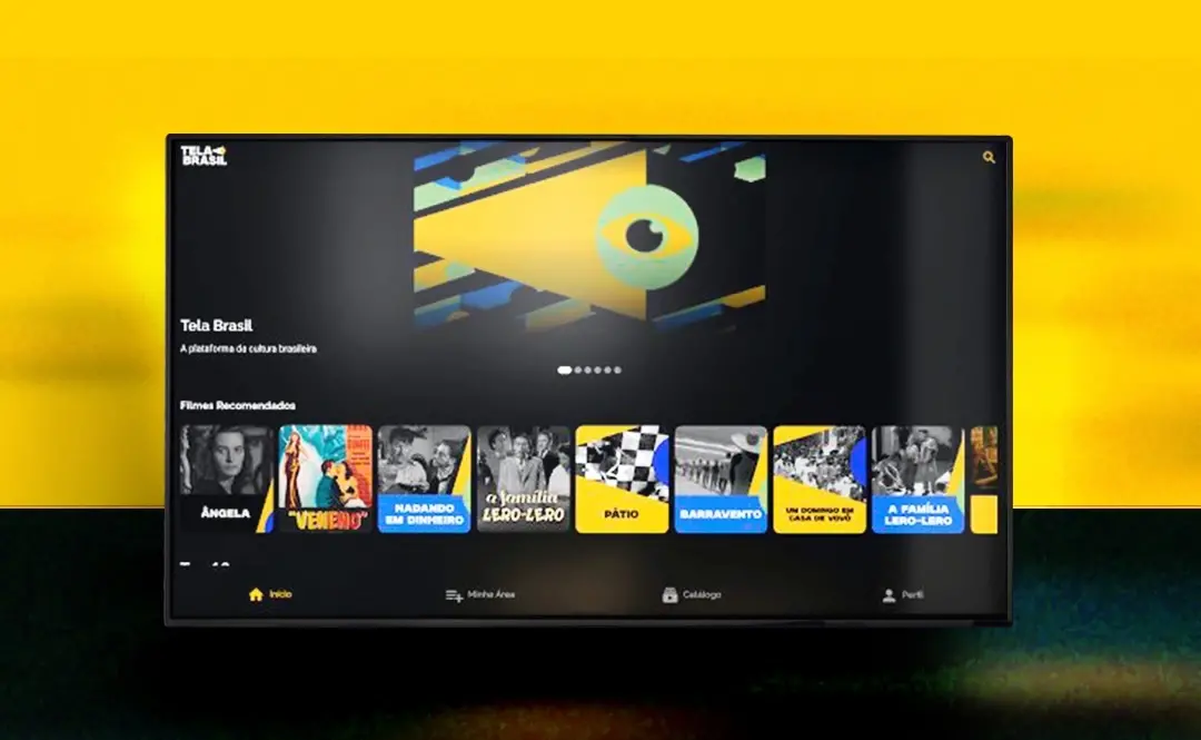 Interface da plataforma de streaming 'Tela Brasil' é exibida em uma tela, destacando um banner central abstrato com a ilustração de um olho em tons de amarelo e verde. Abaixo do banner, uma fileira horizontal apresenta miniaturas de filmes recomendados, como 'Ângela', 'Veneno' e 'Barravento', sobre um fundo escuro integrado a um cenário externo texturizado.