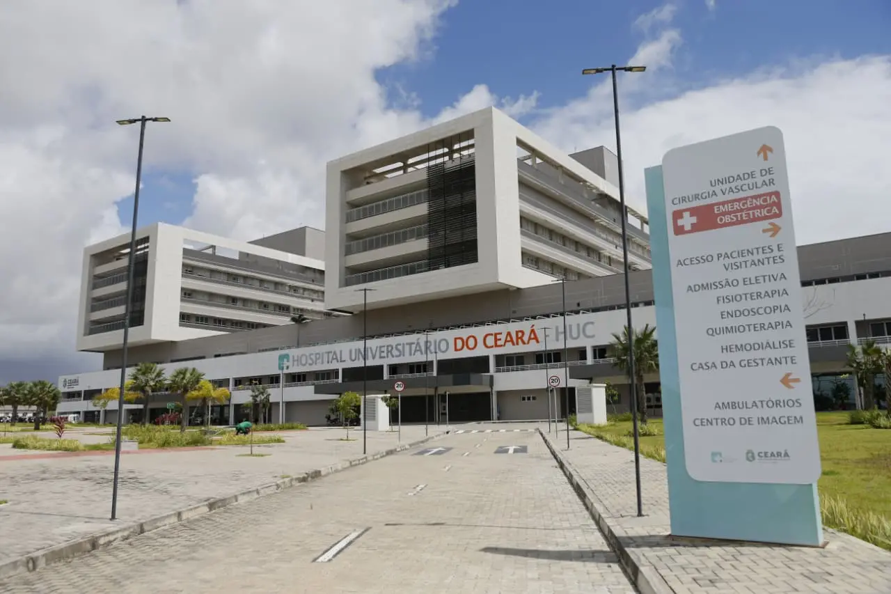 Fachada principal do Hospital Universitário do Ceará (HUC), em Fortaleza. A imagem mostra a entrada da Emergência Obstétrica do hospital público do SUS, com letreiros do Governo do Estado do Ceará e da Secretaria da Saúde (Sesa), além do estacionamento em primeiro plano.