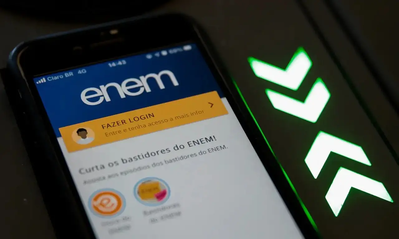 Celular exibindo a tela do app ENEM com a mensagem “Fazer login” e, ao lado, um tablet com o ícone verde em formato de seta e texto “ENEM”, em ambiente escuro.