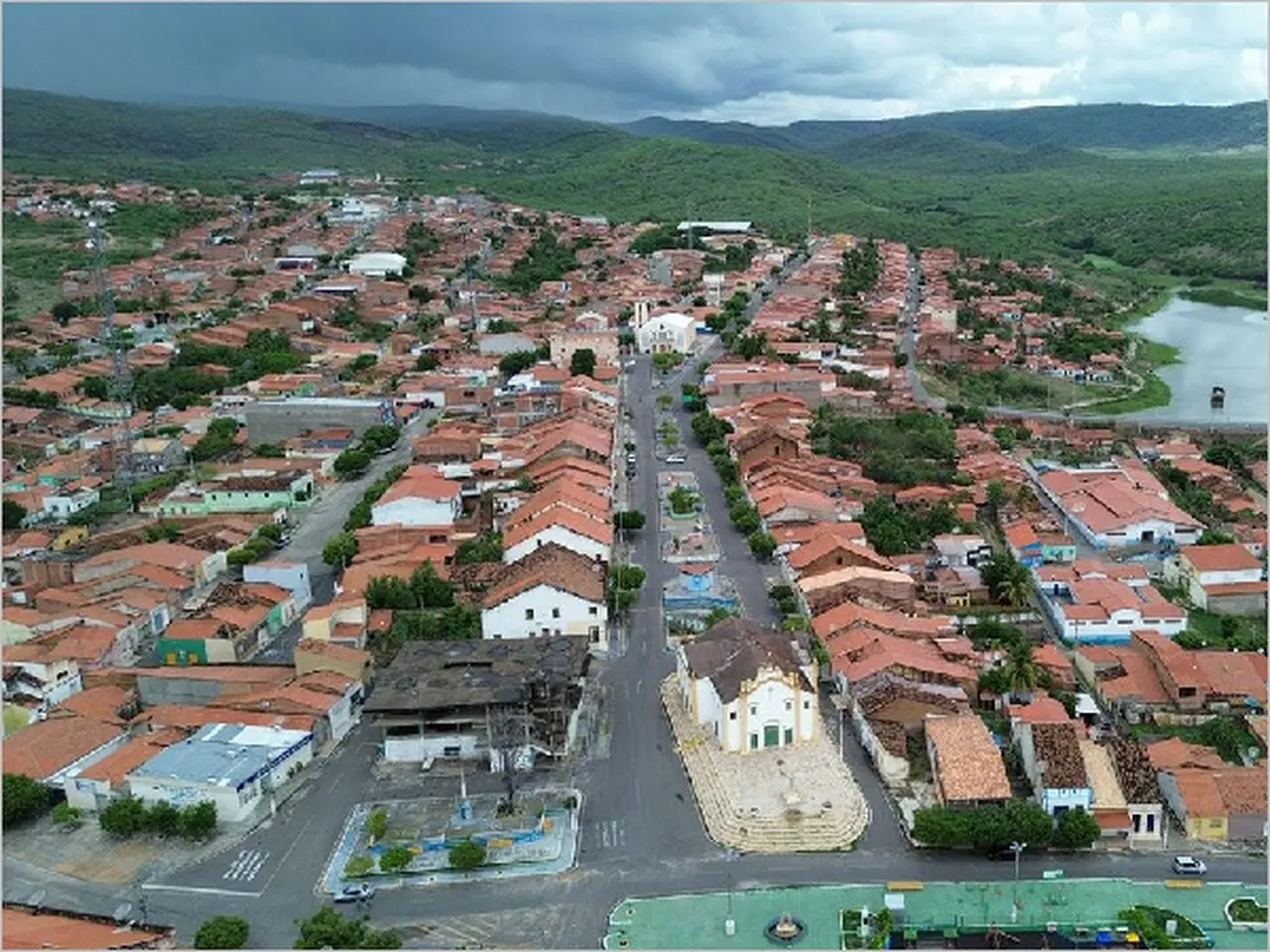Imagem aérea de cidade, com diversas casas com telhas e paisagem verde ao fundo.