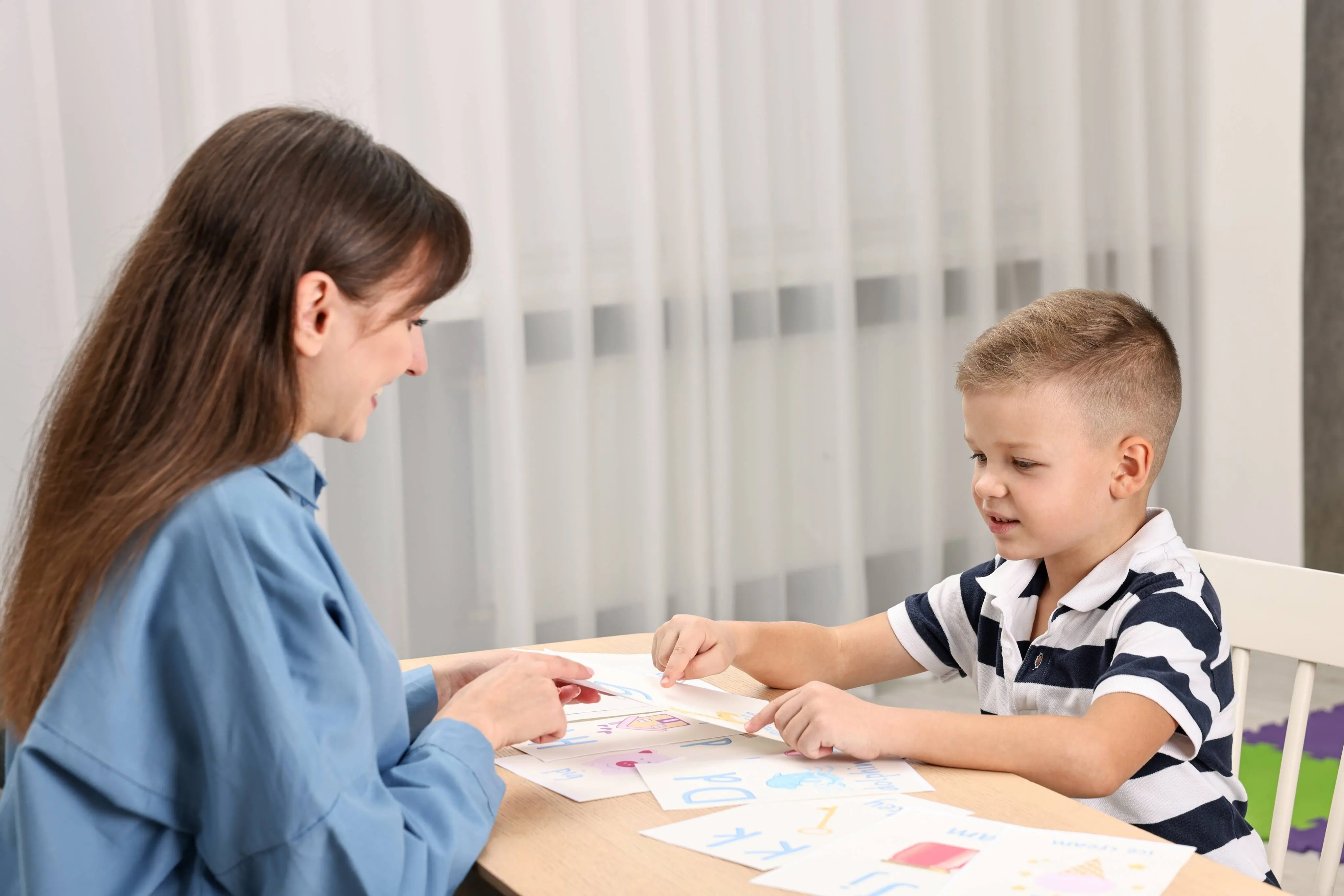 Imagem de uma mulher trabalhando com comunicação alternativa com uma criança para matéria sobre autismo.